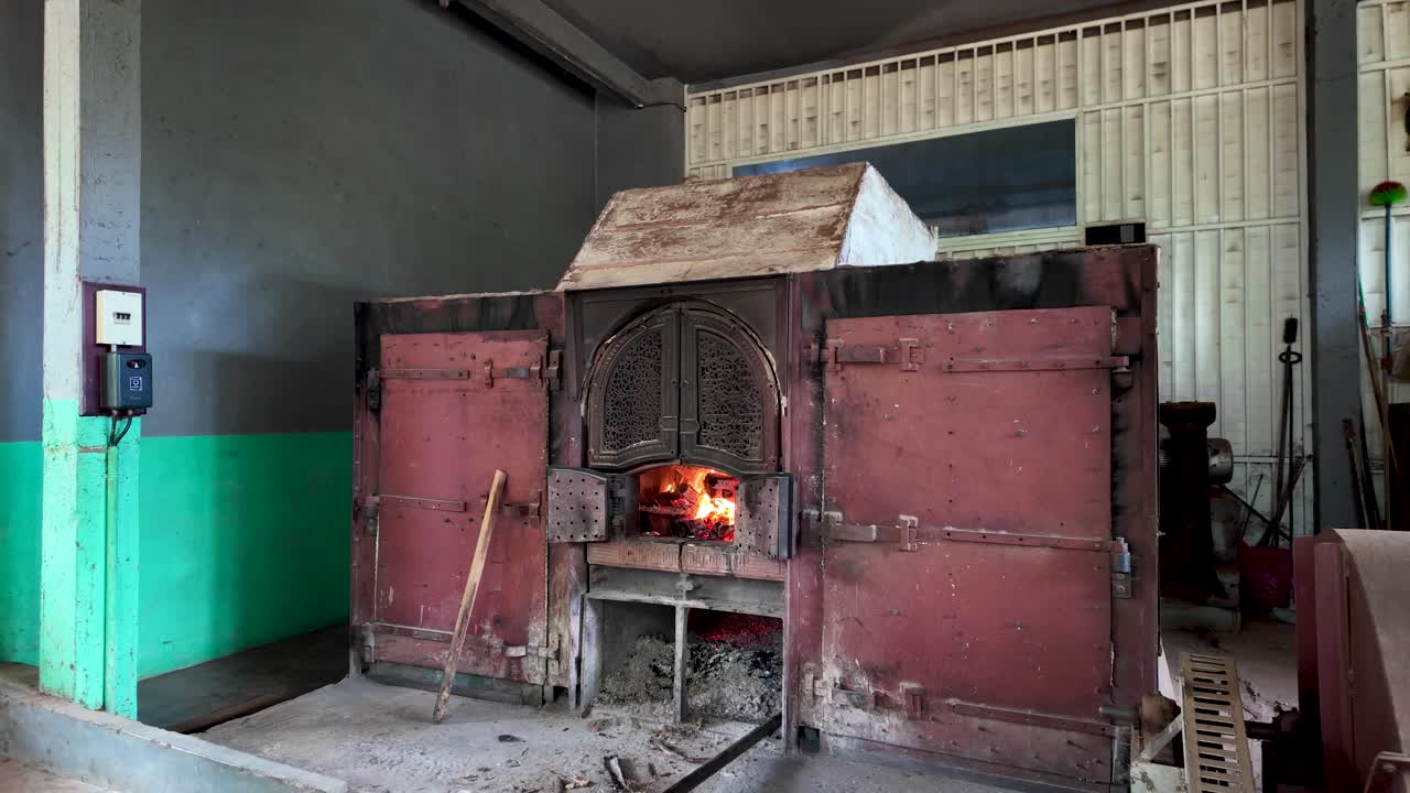 Robust, large rustic wood stove burner situated within an industrial factory environment, showcasing traditional heating methods and industrial design.