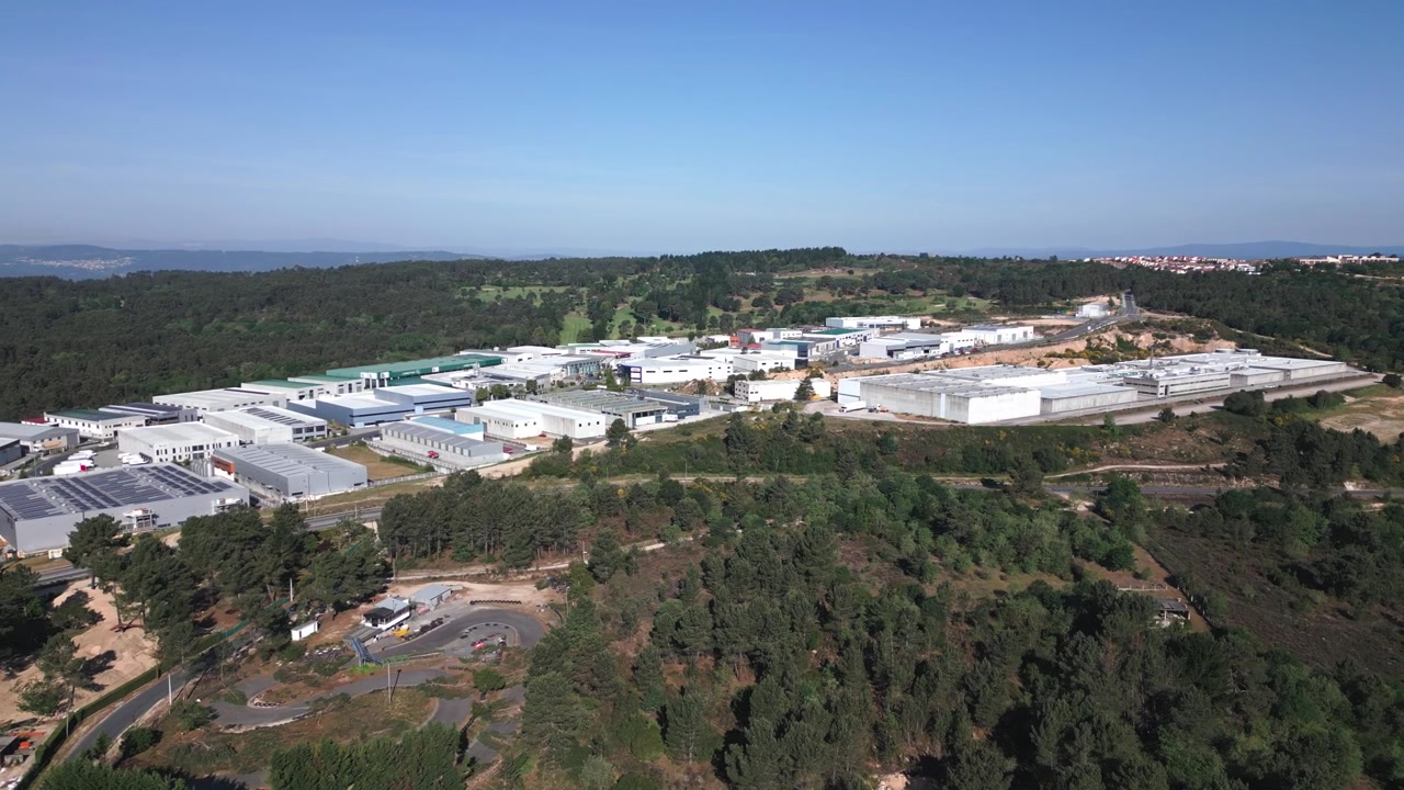 Video drone che mostra un grande parco industriale immerso tra alberi verdi e lussureggianti, piena luce del giorno, cieli sereni e vaste strutture moderne