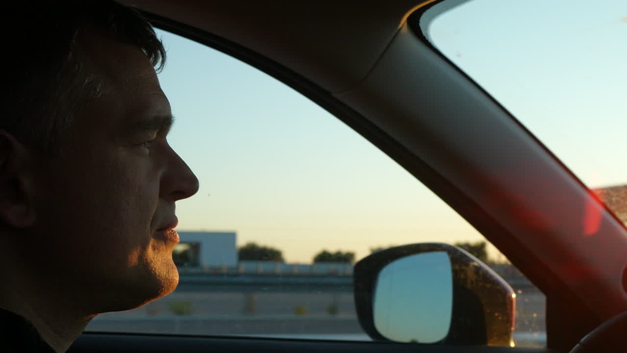 Man driving car looking outside window at sunset