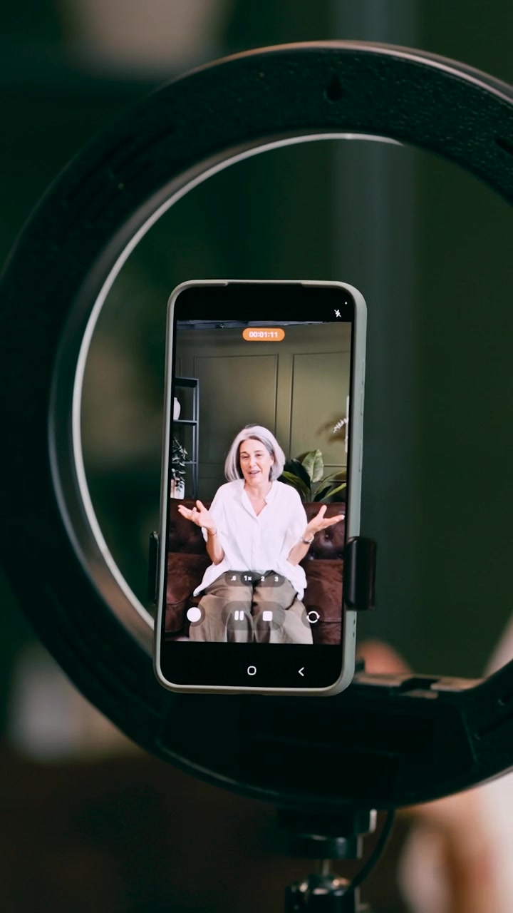 Donna matura che registra contenuti video sullo smartphone con una ring light