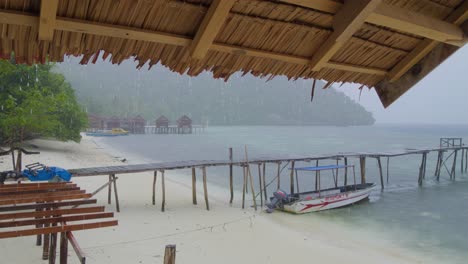 la lluvia tropical en la isla de kri en el archipiélago de raja ampat, mientras cae en cascada sobre el mar y la playa de arena, vista desde el refugio de la cabaña de madera