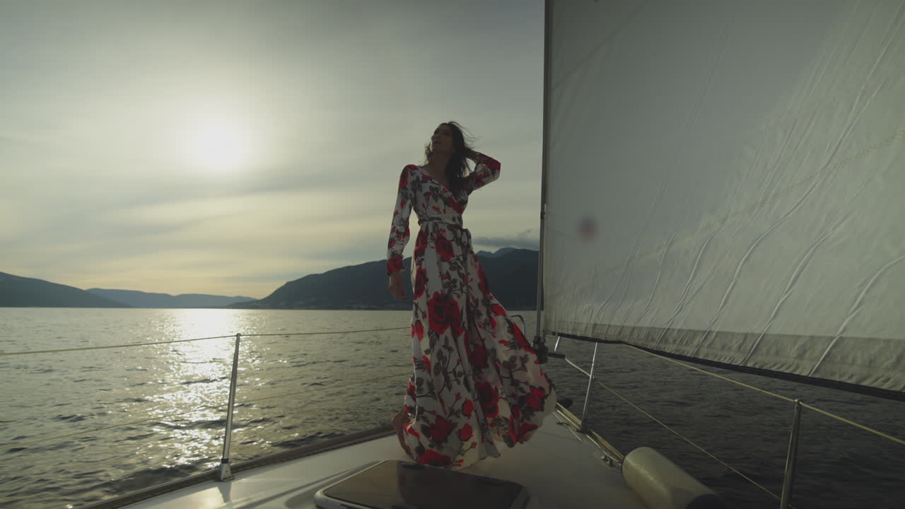 mujer en un vestido floral en un yate de vela al atardecer