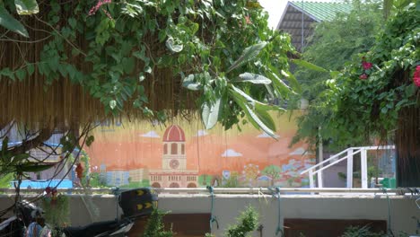 a beautiful street wall painting of the church of santa cruz, thailand - obstructed view behind a tree - tilt down