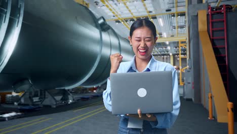 happy asian business woman celebrating using laptop computer in pipe manufacturing factory