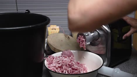 woman grinding pork for meatball mass with the electric mincer in a kitchen, slow motion