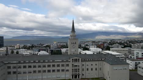 Eine-4K-Drohne-Gleitet-über-Das-Herz-Von-Reykjavik,-Während-Der-Große-Glockenturm-Als-Wache-Vor-Der-Ruhigen-Uferpromenade-Steht