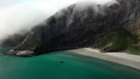 Aerial-footage-of-a-boat-in-clear-blue-waters-at-the-island-of-Vaeroy,-Lofoten-Islands-in-Norway