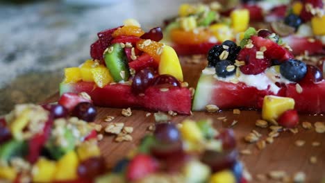 panning shot over slices of watermelon with a yogurt cream on top along with granola and a variety of fruits including blueberries, pineapple, strawberries, and raspberries