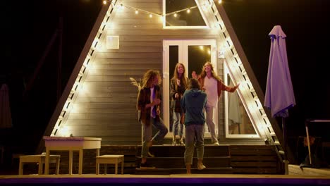 a company of two boys and two girls dance together against the background of glowing lights. resting at a party outside the city. rest in the country house