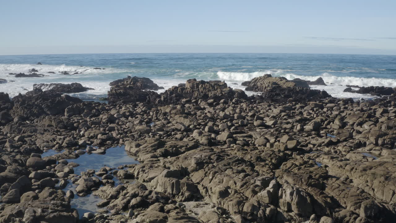 Slow 4K high detail pull in over California's rocky coast in Monterey Bay with tide pools and breaking waves visible