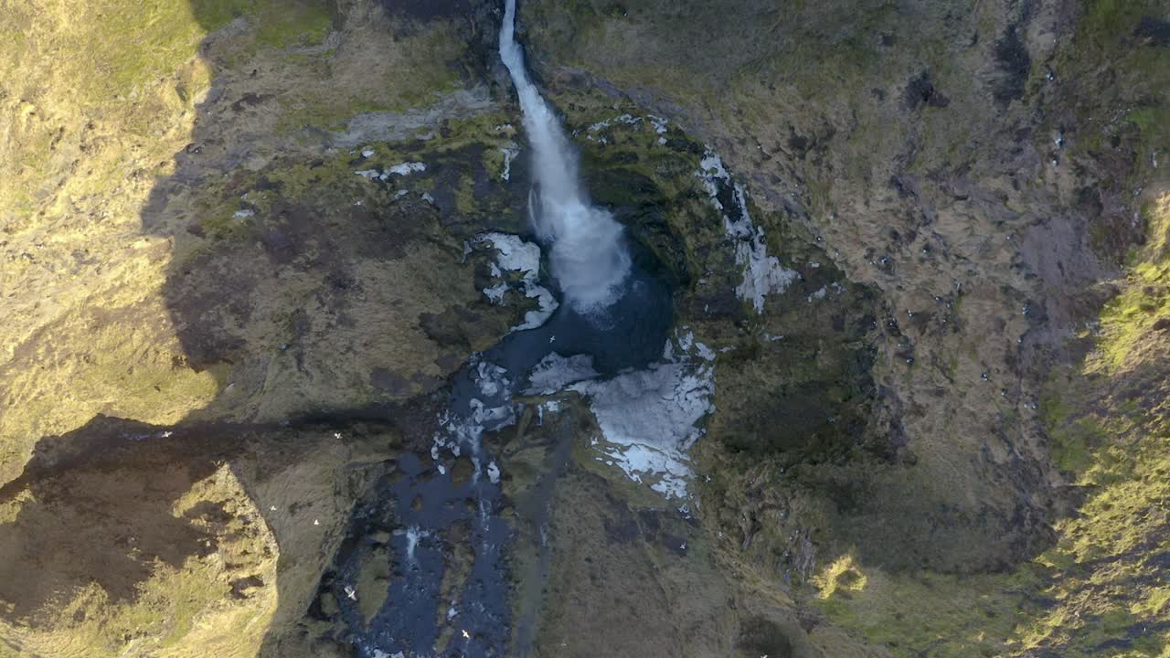Flying slow motion towards a waterfall in Iceland looking straight down.