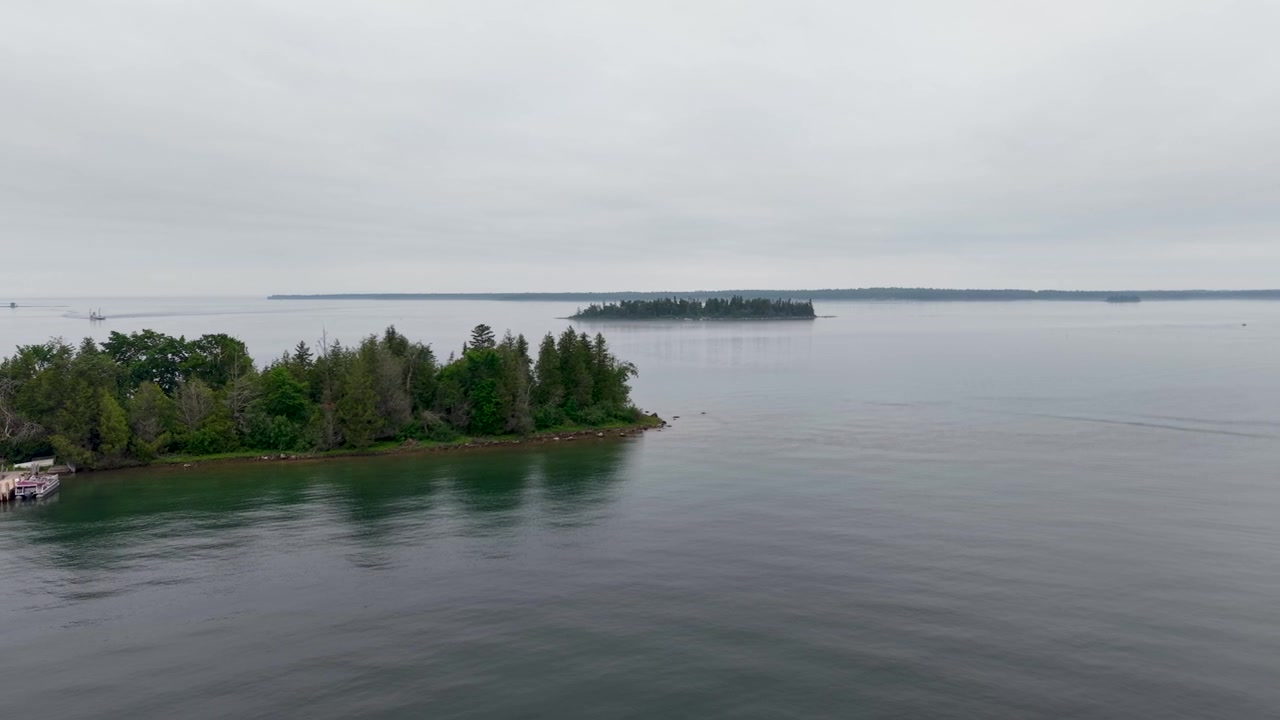 Vista aérea de drone enquadra uma península arborizada e uma ilha distante sobre as águas calmas e cinzentas do Lago Huron.