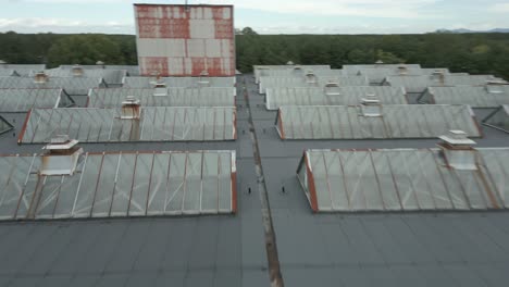 Fast-Aerial-fly-over-rooftop-with-glass-windows-in-factory-complex