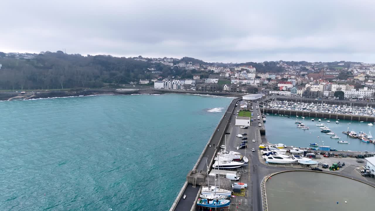 Guernsey St Peter Port.Flight from seaward over model yacht pond towards Havelet Bay showing breakwater, fishermans quay and Albert Marina with town as a backdrop on cloudy day.