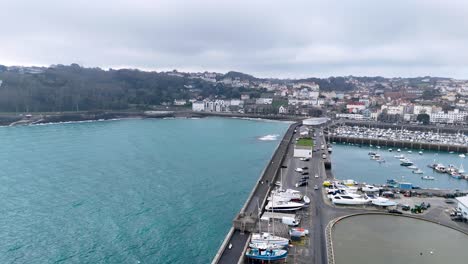 guernsey st peter port.flight from seaward over model yacht pond towards havelet bay showing breakwater, fishermans quay and albert marina with town as a backdrop on cloudy day.