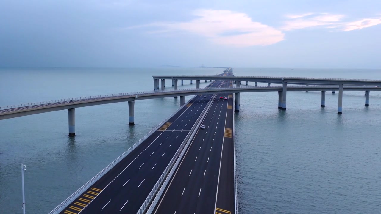 Droneoptagelse i aftentusmørke af Qingdao tværgående motorvej over havet, med kørende trafik og logistiklastbiler på en gigantisk bugtbro, et vartegn for kystinfrastrukturen i Shandong, Kina