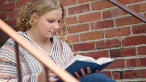 Girl reads a book outside on stairs next to a brick wall