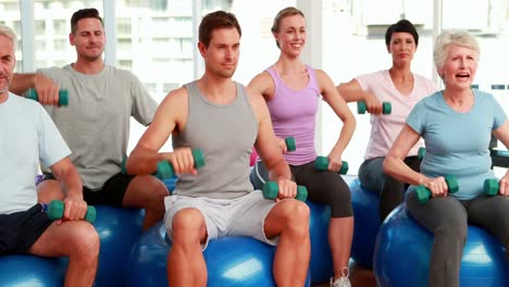 Fitness-group-sitting-on-exercise-balls-lifting-hand-weights