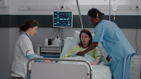 nurse with dark skin helping patient to sit comfortable in hospital ward
