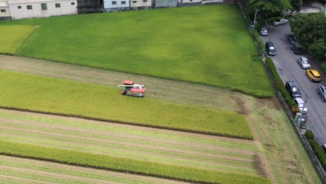 Aerial-drone-footage-Cultivated-rice-paddy-field,-farmer-harvesting-the-crops-with-multifunctional-paddy-harvesting-machine-rice-harvester-tractor-at-Doliu-Yunlin-Taiwan