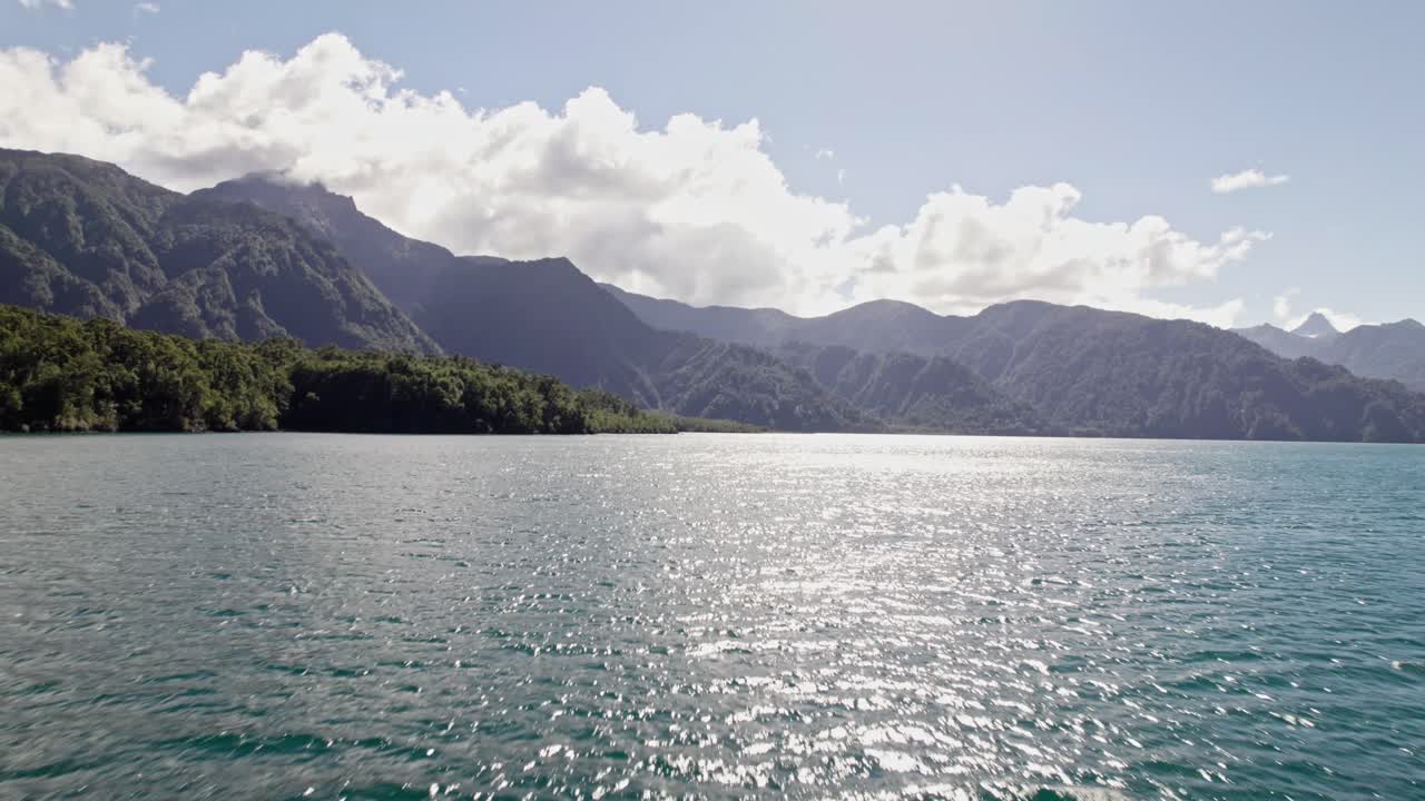 Wide panoramic view of the deep blue, pristine waters of Lago Todos Los Santos (Emerald Lake) framed by dense forest and towering mountains in Vicente Pérez Rosales National Park, Chile