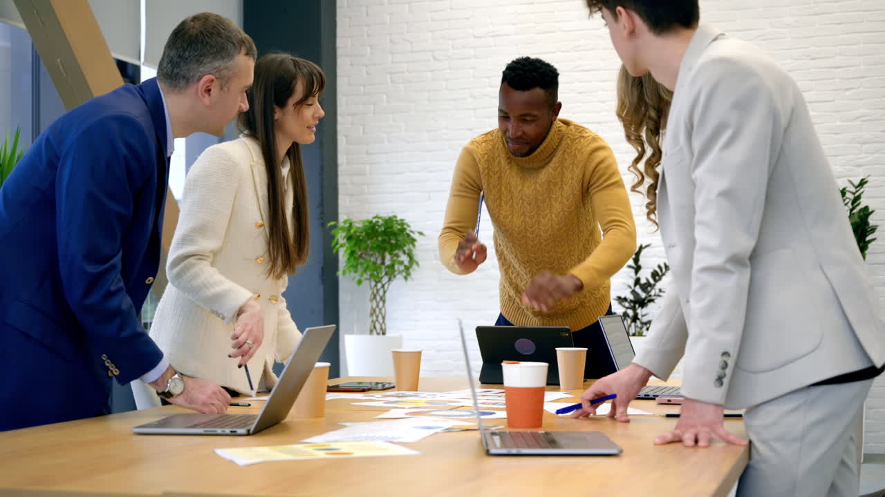Black male team leader at business meeting in an office, discussing business affairs with other workers, papers and gadgets on the table