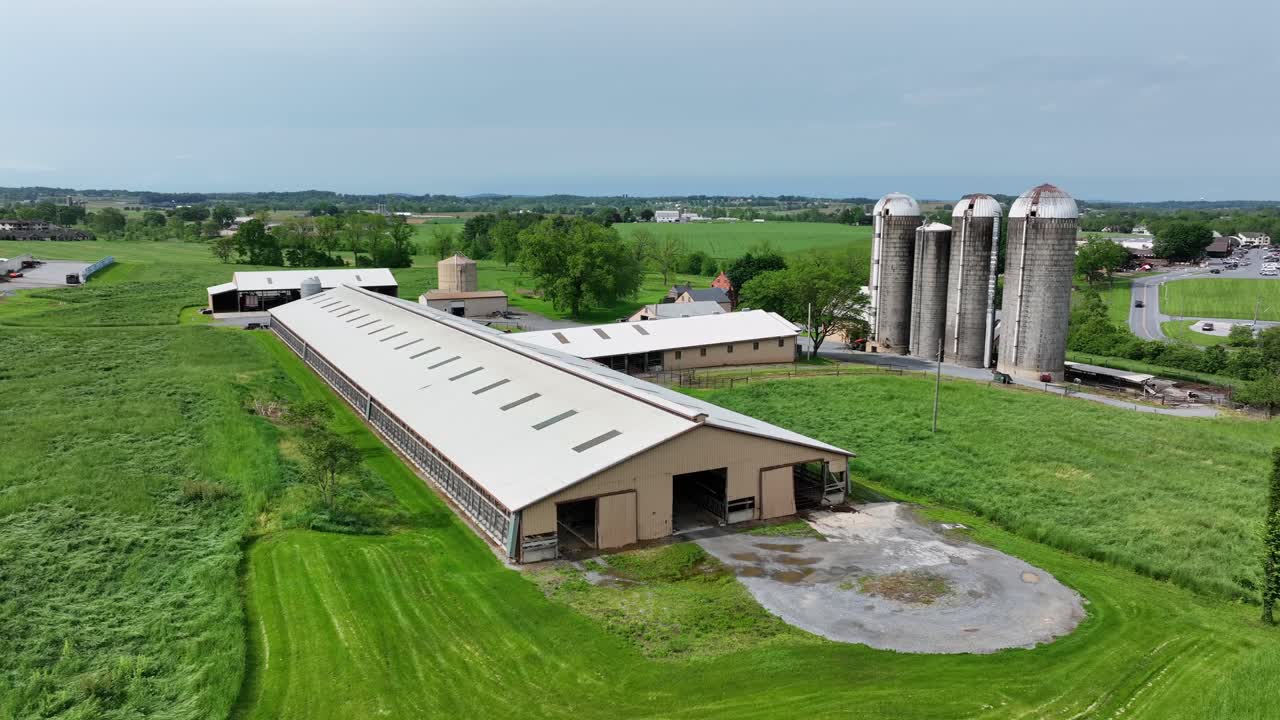 American farm, showcasing large barns and towering silos surrounded by lush green fields. Agricultural landscape and rural atmosphere during sunny spring day in midwest of america. Aerial view.