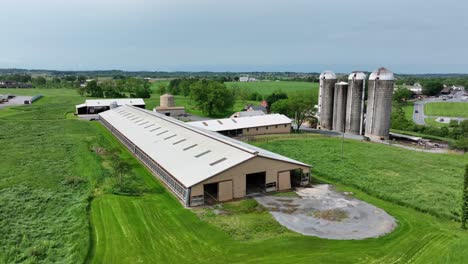 american farm, showcasing large barns and towering silos surrounded by lush green fields. agricultural landscape and rural atmosphere during sunny spring day in midwest of america. aerial view.