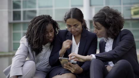 enthusiastic colleagues looking at smartphone and gossiping