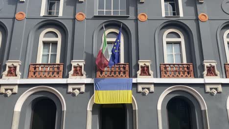Ukrainian-national-official-flag-and-italian-and-europe-flags-are-waving-in-the-wind-from-the-balcony-Historical-building-in-Italy