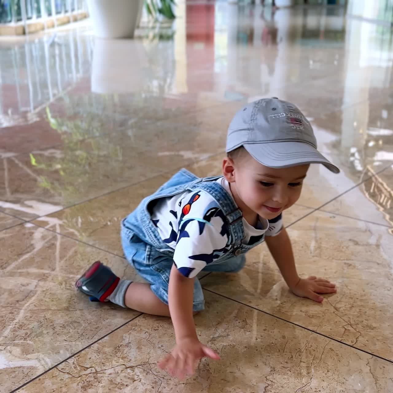 Bambino adorabile con un cappello che cade sulle ginocchia nel centro commerciale. Un bimbo felice gattona per terra giocando.