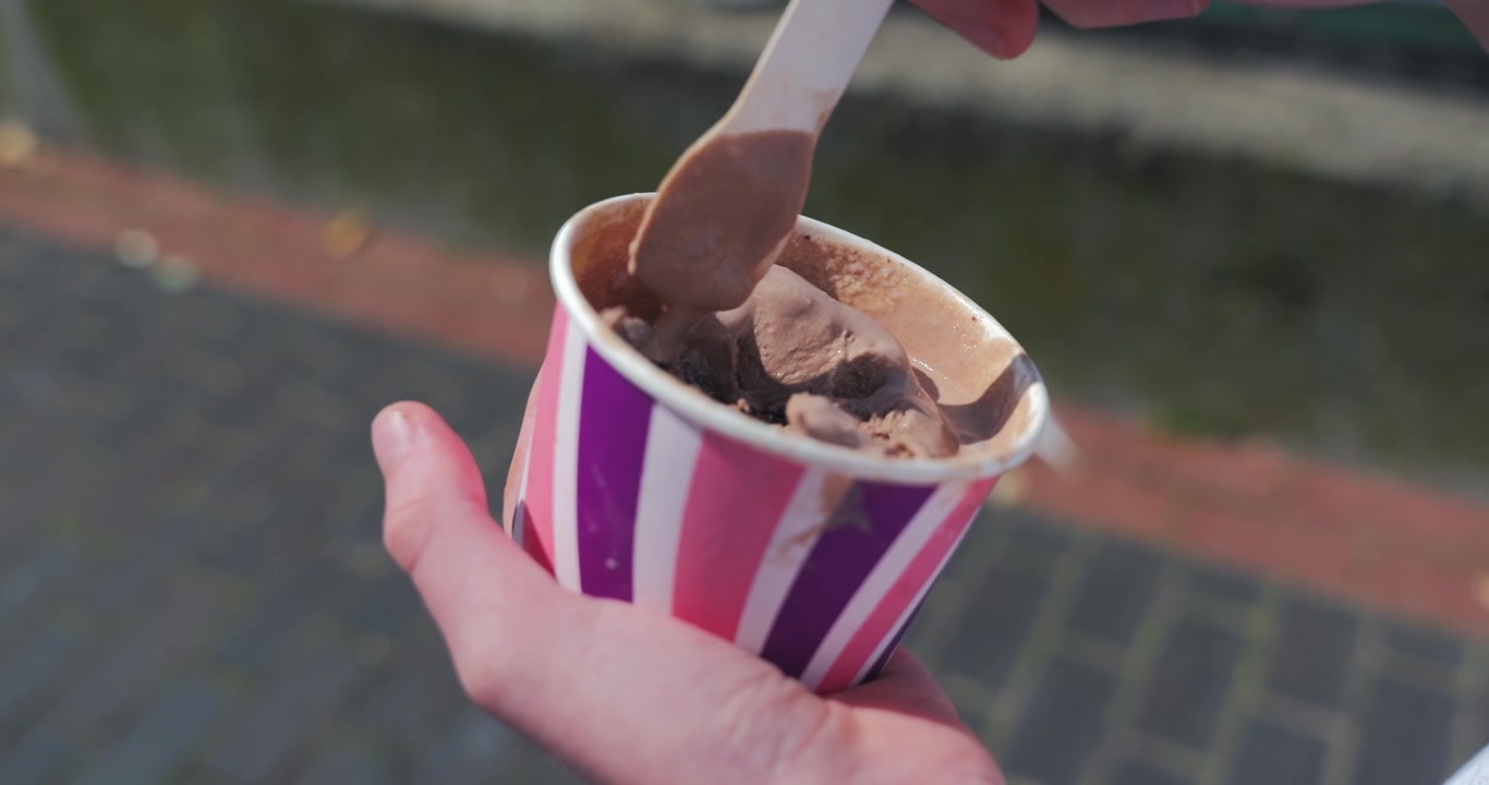 Primo piano di una persona che mangia gelato al cioccolato vicino al porto in una giornata di sole.