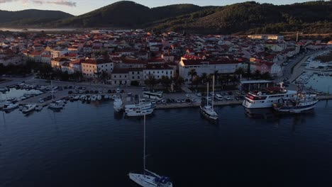 Early-morning-drone-flight-over-quiet-harbour-with-cars-flying-diagonally-over-houses-on-croatian-island