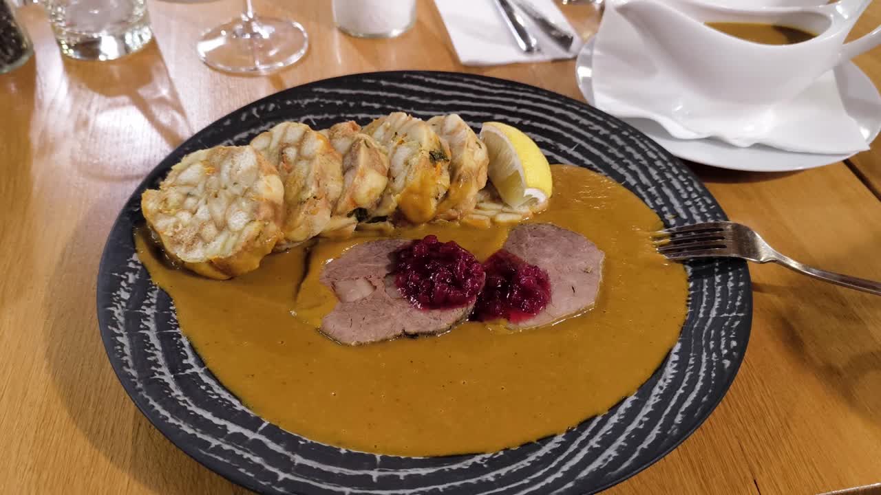 Classic Czech dish of sausage, beef, and dumplings in cream sauce, served on an ornate black plate, slow gradual pullback