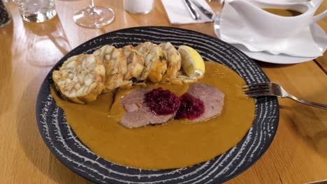 classic czech dish of sausage, beef, and dumplings in cream sauce, served on an ornate black plate, slow gradual pullback