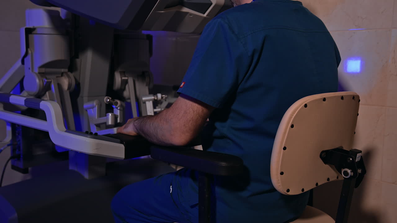 Male surgeon in blue uniform takes place in front of equipment. Specialist takes the handles of robotic device to rule the machine.