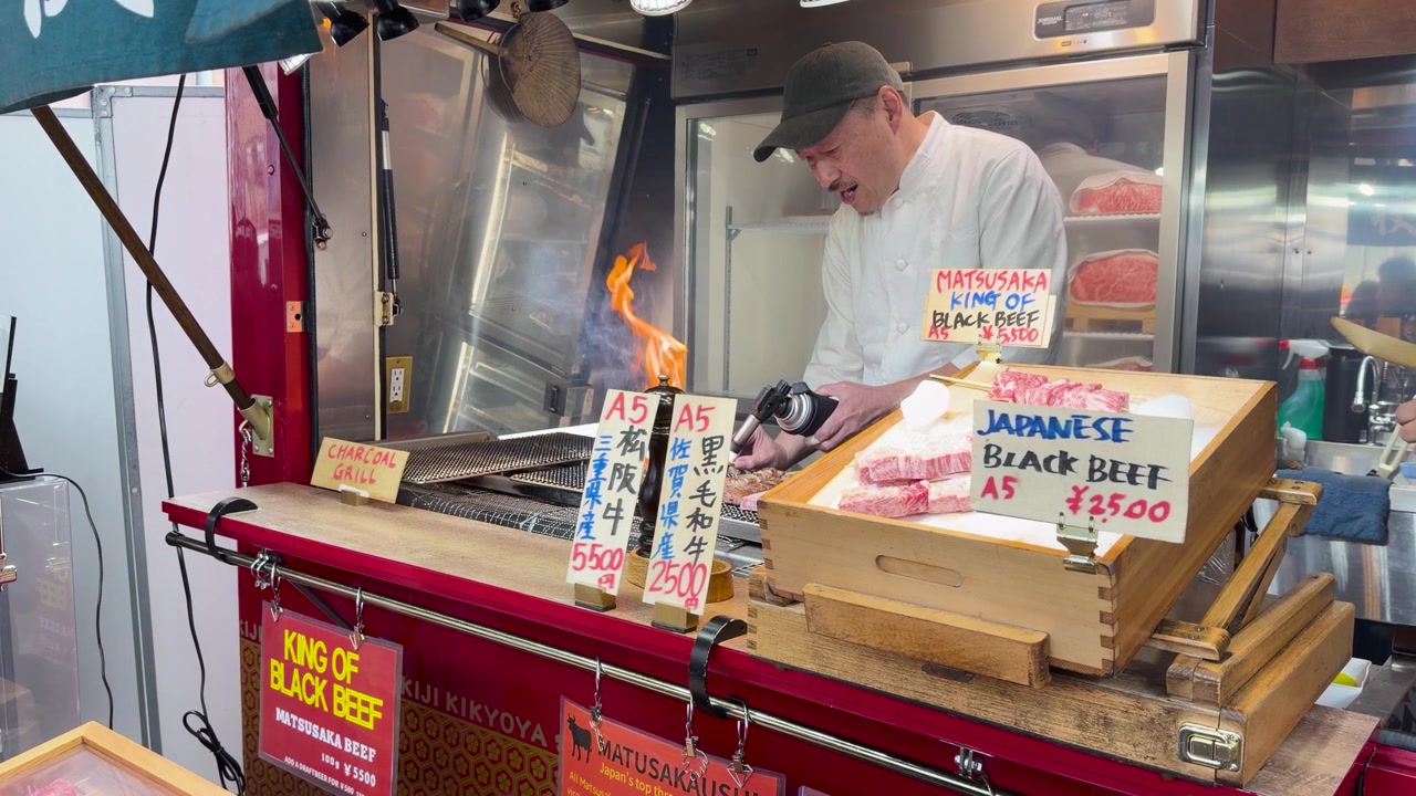 Ein Koch verwendet einen Bunsenbrenner, um hochwertiges Wagyu-Rindfleisch an einem Straßenstand in Tokio anzubraten.