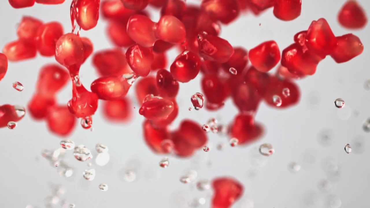 Red Pomegranate Seeds and Water Droplets Falling in Slow Motion