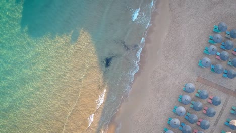 forward moving drone over the sea waves reaching the tourist beach with shacks arranged systematically