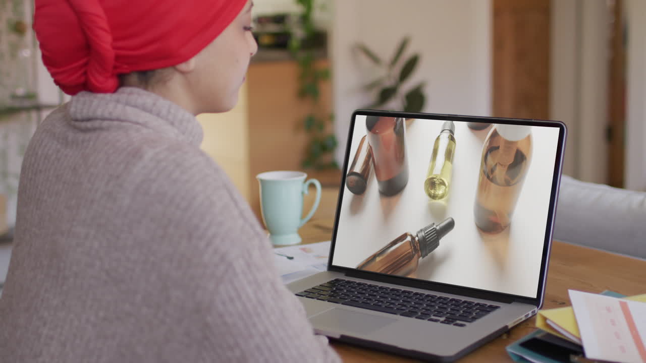 Kvinde af blandet etnicitet ved bord bruger bærbar computer, handler skønhedsprodukter online, i slow motion.