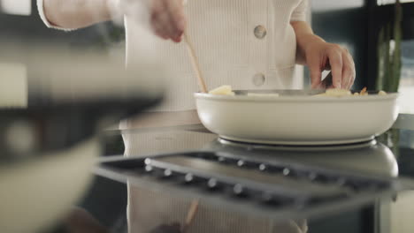 a woman fries potatoes on an induction electric stove with a built-in extractor fan