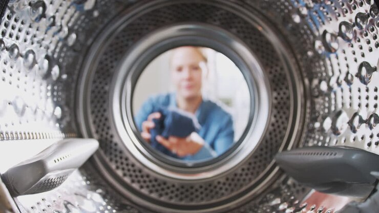 View Looking Out From Inside Washing Machine As Woman Puts In Laundry Load