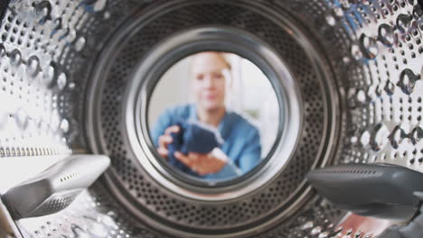 view looking out from inside washing machine as woman puts in laundry load