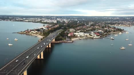 aéreo: disparo de un dron que sigue a los automóviles que cruzan un puente hacia un suburbio frente al mar en sydney, australia