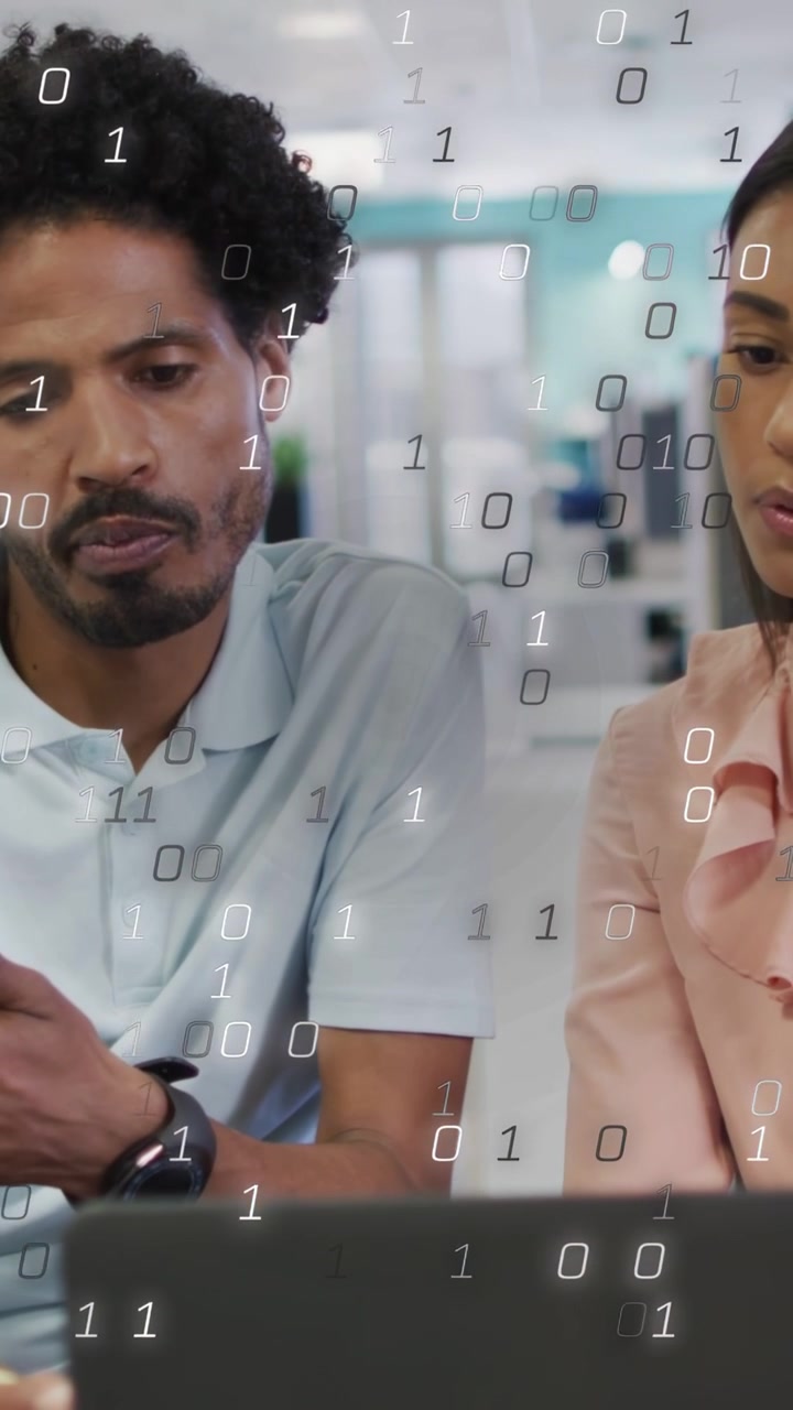Vertical video: Tech team viewing laptop while man tapping phone, causing binary overlay for review