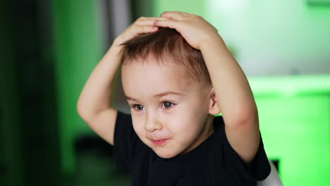 lovely cute caucasian toddler eating and waving hands happily. baby boy puts his hands on head and smiles adorably. close up. blurred backdrop.