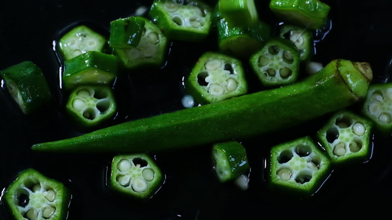 Cinematic slow motion footage of okra or lady's fingers being tossed on a dark and wet working surface