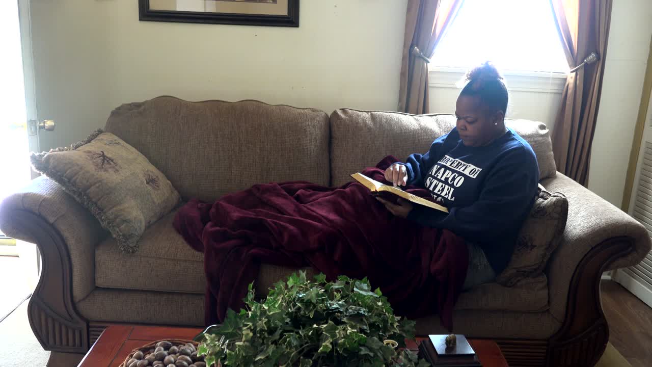 African American woman sitting comfy on couch reading bible