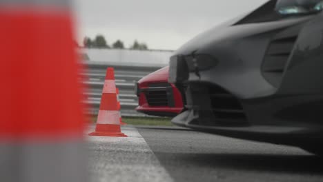 Rotes-Und-Schwarzes-Auto-Bereit-Zum-Start-Des-Drag-Rennens,-Das-Hinter-Der-Startlinie-Wartet,-Mit-Hütchen-Im-Vordergrund-In-4k