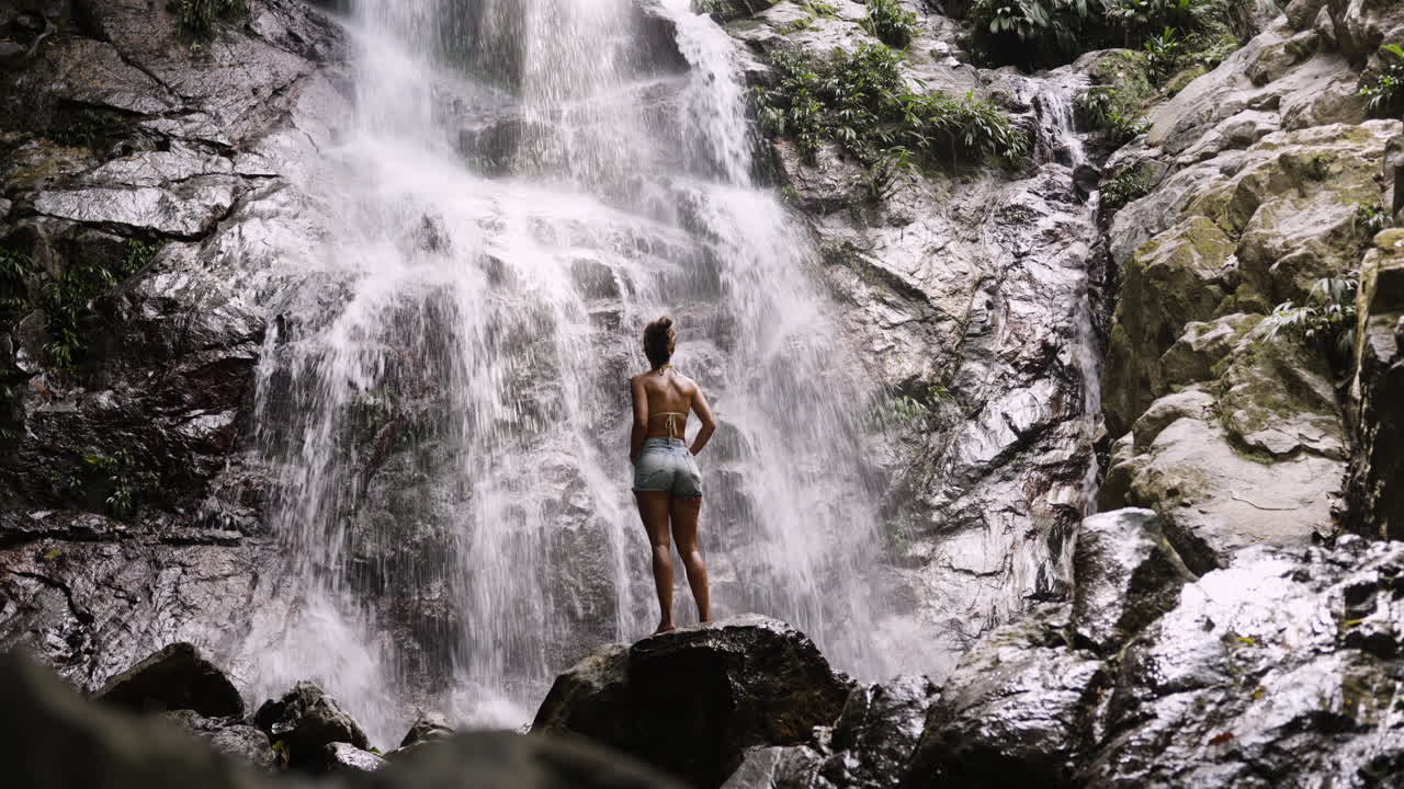 Girl at waterfall, mist rising around her in lush Colombian jungle setting
